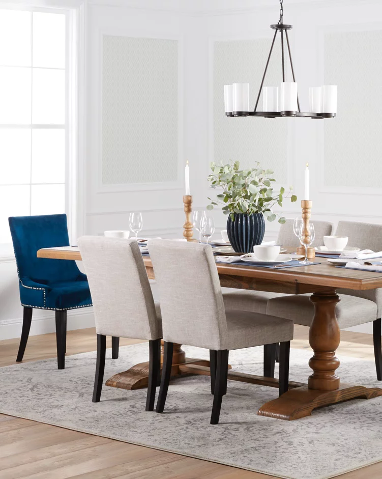 A transitional dining room with a beautiful wooden trestle table, upholstered seating, blue velvet end chairs, an industrial chandelier and a dining table area rug. Links to DX Offers Mall's dining room furniture and decor